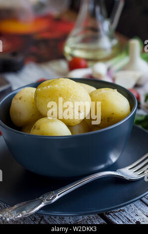 Tasty Young boiled potatoes with dill, sparsley and onions in black bowl on white rustic wooden table Stock Photo