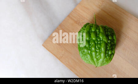 A green round hybrid bitter gourd, placed on a wooden cutting board.