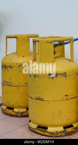 Two metal gas cylinders in yellow, containing liquefied petroleum gas, also referred to as propane. These are used as cooking gas in kitchen. Stock Photo