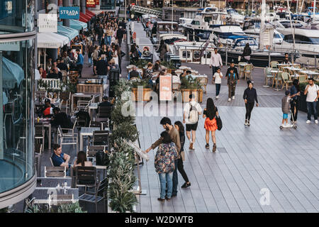 London, UK - June 22, 2019: People walking past restaurants and cafes in St. Katharine Docks, a former dock converted into marina and mixed-used comme Stock Photo