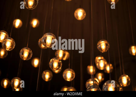 Decorated electric garland for lighting with bulbs warm white and yellow light on a dark background. Blurred background. Bulbs in the interior decor. Stock Photo