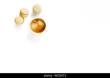 White cup of tasty coffee on white isolated desk with three yellow macarons. Stock Photo