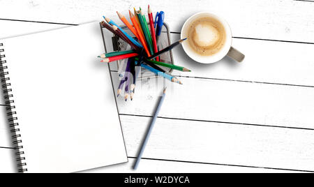 top view of box filled with colored pencils and sketchbook or spiral notepad on rustic white wooden table Stock Photo