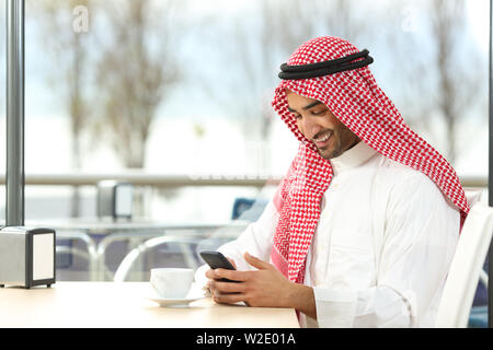 Happy arab man using a smart phone sitting in a coffee shop interior Stock Photo