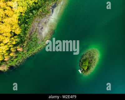 Aerial top down view of a small island. Birds eye view of beautiful green waters of lake Gela surrounded by pine forests. Clouds reflecting in Gela la Stock Photo