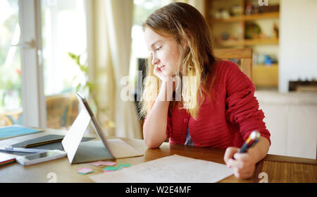 Smart preteen schoolgirl doing her homework with digital tablet at home. Child using gadgets to study. Education and learning for kids. Stock Photo