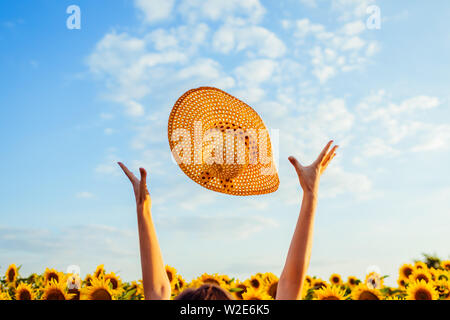 Young woman walking in blooming sunflower field throwing hat up and having fun. Summer vacation Stock Photo