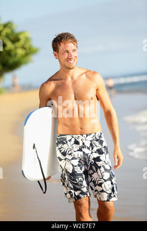 Man on beach holding body surfing bodyboard doing water sports. Summer vacation travel outdoor activity image with handsome fit male fitness sport model smiling happy on tropical beach. Stock Photo