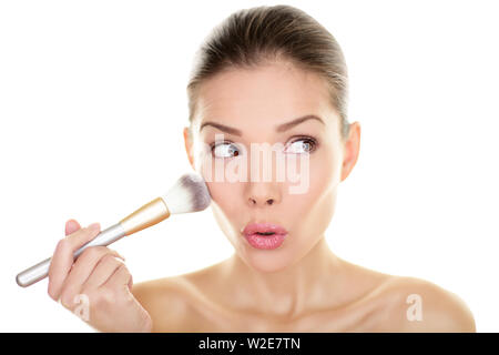 Makeup blush beauty woman looking funny away to side. Surprised cute adorable girl applying make-up on cheeks make up brush looking sideways. Mixed race Asian Chinese / Caucasian model 20s Isolated. Stock Photo
