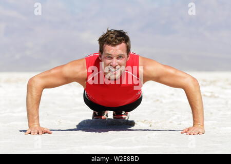 Fitness man doing push ups training outdoor in wild hot desert landscape. Determined strong male athlete doing cross fit training push up outside showing strength and determination. Stock Photo