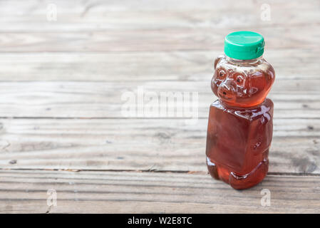 Healthy organic natural sweetener, raw honey - from bees. Golden brown liquid in bear shaped bottle with green cap. Isolated on solid wooden backgroun Stock Photo
