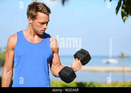 Bicep curl - weight training fitness man outside working out arms lifting dumbbells doing biceps curls. Male sports model exercising outdoors as part of healthy lifestyle. Stock Photo