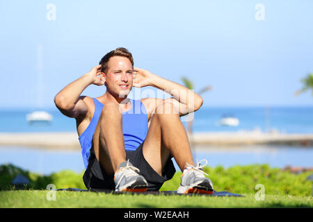 Man exercising sit-ups outside. Male fitness model training situps exercise outdoor in summer during workout. Handsome fit muscular sport model. Stock Photo