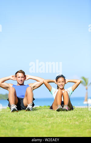 People exercising - Couple doing sit ups outdoors. Fitness couple doing situps exercise during outside cross training workout. Happy young multiracial couple, Asian woman, Caucasian man. Stock Photo