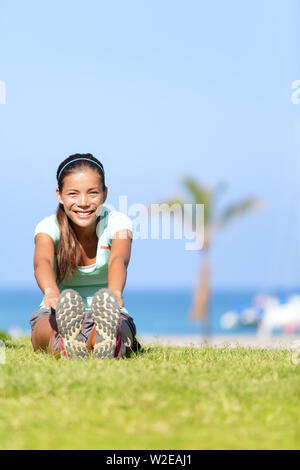 Fit fitness woman doing stretching exercises outdoors. Girl doing hamstring leg stretching exercise and stretches. Female sports model exercising outdoor in summer. Beautiful multiracial Asian girl. Stock Photo