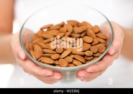 Almonds nuts - woman showing raw almond bowl close up. Healthy food concept in studio with hands lifting bowl of unprocessed almonds isolated on white background. Stock Photo