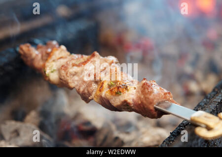 Spit roasted meat being cooked on a charcoal grill Stock Photo