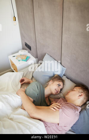 Happy young amorous spouses looking at one another while lying in bed Stock Photo