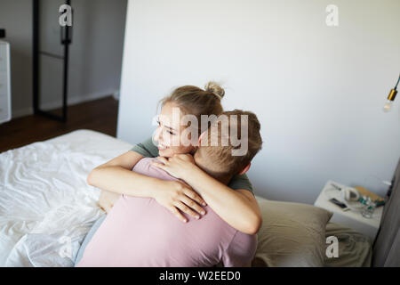 Cheerful young woman embracing her husband while both sitting on bed in the morning Stock Photo