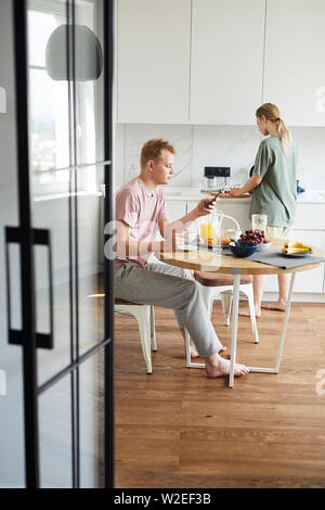 Casual guy having coffee by served table and texting in smartphone during brunch in the morning Stock Photo