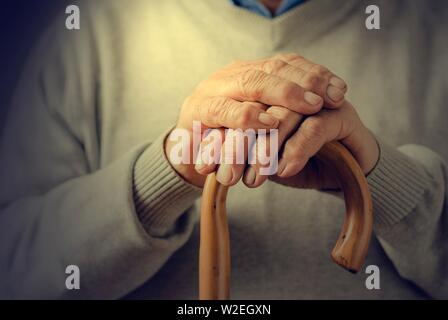 Close up details of the folded hands of an elderly man resting on a walking cane in a mobility and health concept Stock Photo