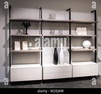 Display cabinet in a modern living room with open shelves housing ceramics and ornaments against a white wall in a neutral interior home decor Stock Photo