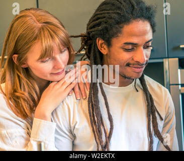 Interracial couple formed by African and Caucasian prepare a salad together with the help of their cell phone Stock Photo