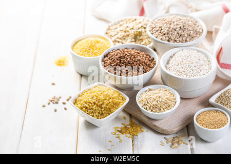 Selection of whole grains in white bowls - rice, oats, buckwheat, bulgur, porridge, barley, quinoa, amaranth, Stock Photo