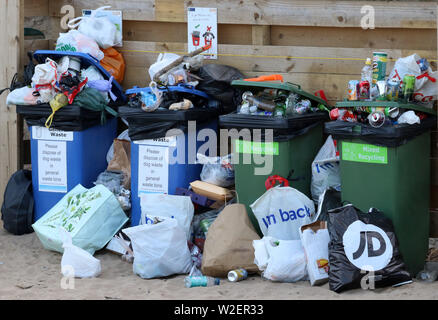 Overflowing recycling wheelie bins awaiting collection on the beach, rubbish litter and  recycling  spilling out of the bins Stock Photo