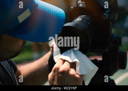 Cropped Hands Of Man Cleaning Camera Lens. Outdoors setup. Stock Photo