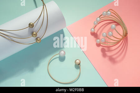 Golden necklace and bracelets with pearls on pastel colors pink and green background Stock Photo