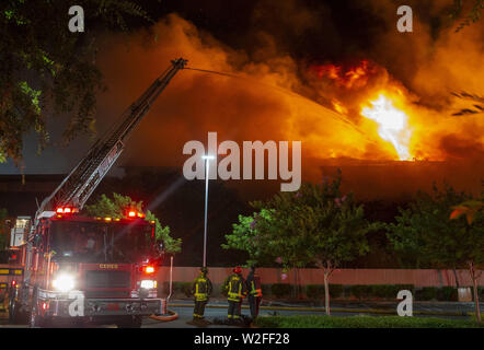 Modesto, CA, USA. 8th July, 2019. One of 5 ladder trucks from Modesto Fire and Ceres Fire Departments shoots water on the north end of the structure. Modesto Fire Department responded to a working structure fire at the corner of Tully Road and 9th Street Tuesday, July 7, 2019 at 9pm. The fire quickly went to multiple alarms bring 3 fire ladder truck along with multiple other engines from throughout Stanislaus County. Credit: Marty Bicek/ZUMA Wire/Alamy Live News Stock Photo