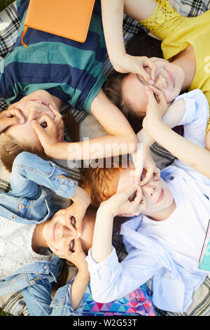 Four school friends chilling in park after school lying on grass outside, having fun and making faces Stock Photo