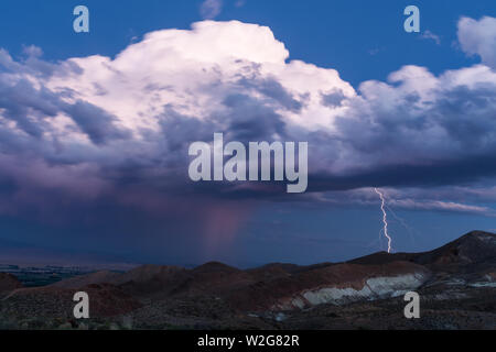 Lightning strikes a mountain at sunset below puffy clouds in the evening Stock Photo