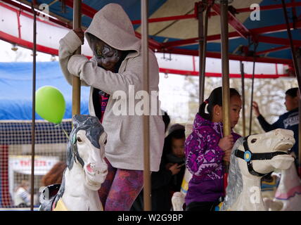 Meriden, CT USA. Apr 2019. Daffodil Festival. African American kid with face at getting on her horse on a merry go round. Stock Photo