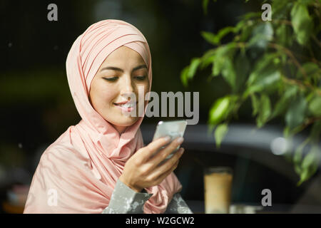 Portrait of young beautiful Muslim woman smiling when reading text message on her smartphone Stock Photo