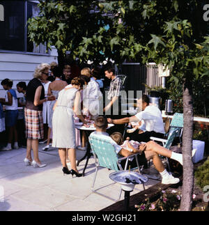 Friends and family enjoying a party on a patio and outdoor picnic ca. 1965 Stock Photo