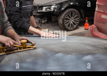Preparation for painting a car element using emery sender by a service technician leveling out before applying a primer after damage to a part of the Stock Photo