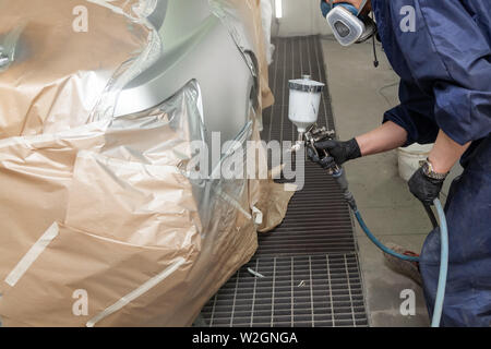 A male worker paints with a spray gun a part of the car body in silver after being damaged at an accident. Rear fender from the vehicle during the rep Stock Photo