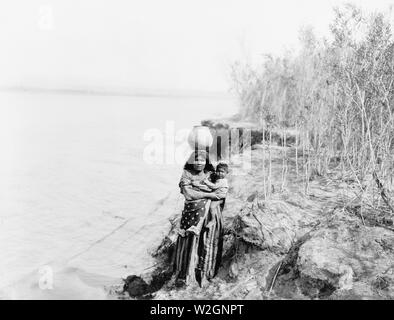 Edward S. Curits Native American Indians - Mohave Indian woman carrying water on her head and holding child ca. 1903 Stock Photo