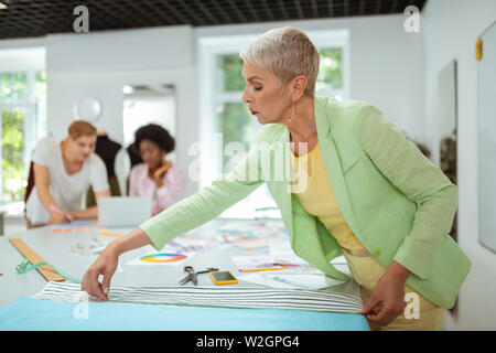 Working process. Elderly woman fashion designer working in a studio using a measuring tape Stock Photo