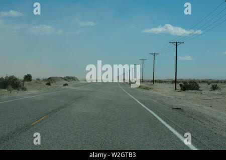 Empty windswept road with blowing sand and bleak feel Stock Photo