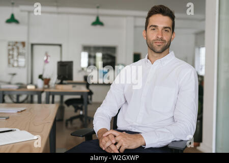 Confident young businessman sitting alone in a large modern office Stock Photo