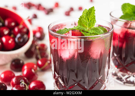 Fresh Cherry Juice in Glasses With Mint Leaves and Ice Cubes, and Fresh Cherries on a Table Close Up on White Background Stock Photo
