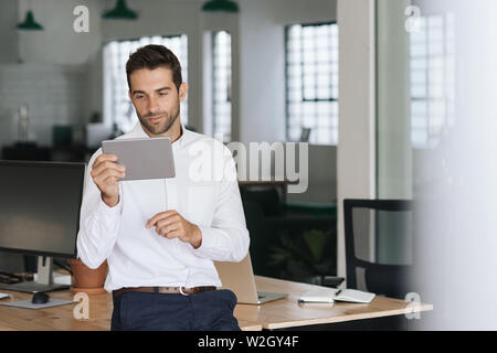 Young businessman leaning on an office desk using a tablet Stock Photo