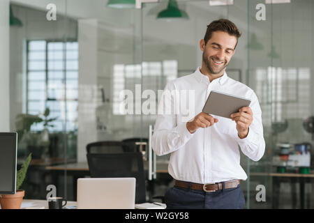 Smiling businessman using a tablet in a large modern office Stock Photo