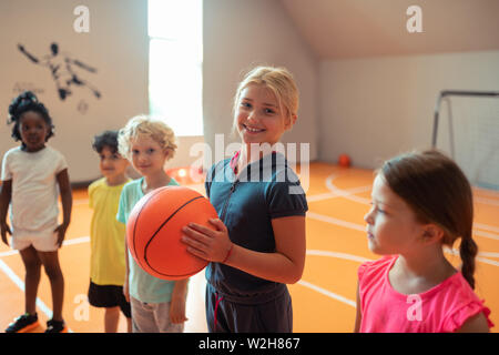 Smiling girl holding a ball standing next to her classmates. Stock Photo