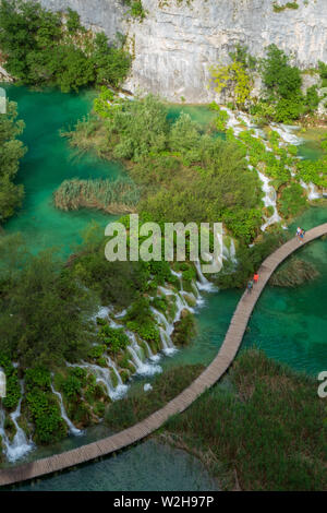 Hikers passing cascades of water rushing down into the azure colored Lake Kaluđerovac at the Plitvice Lakes National Park in Croatia Stock Photo