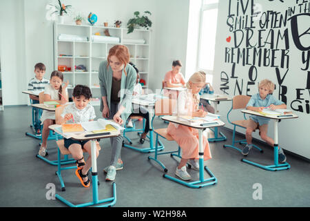 Teacher checking homework of her pupils in class. Stock Photo