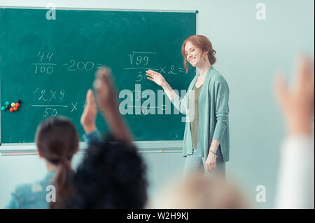 Teacher explaining sums standing near the blackboard. Stock Photo